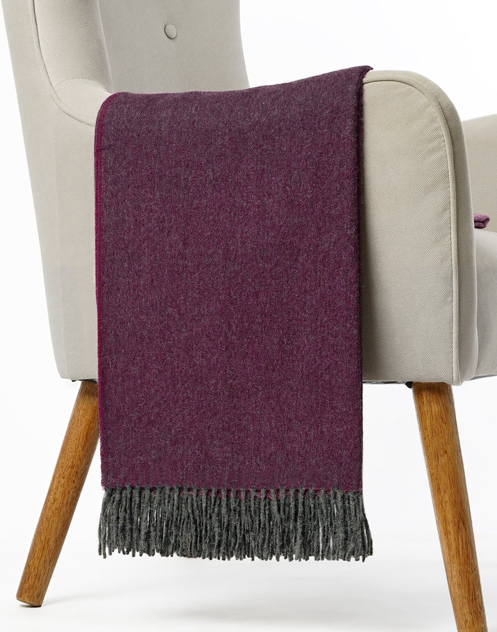 Manta Espiga de baby alpaca en gris medio con detalles púrpura, presentada doblada sobre respaldo