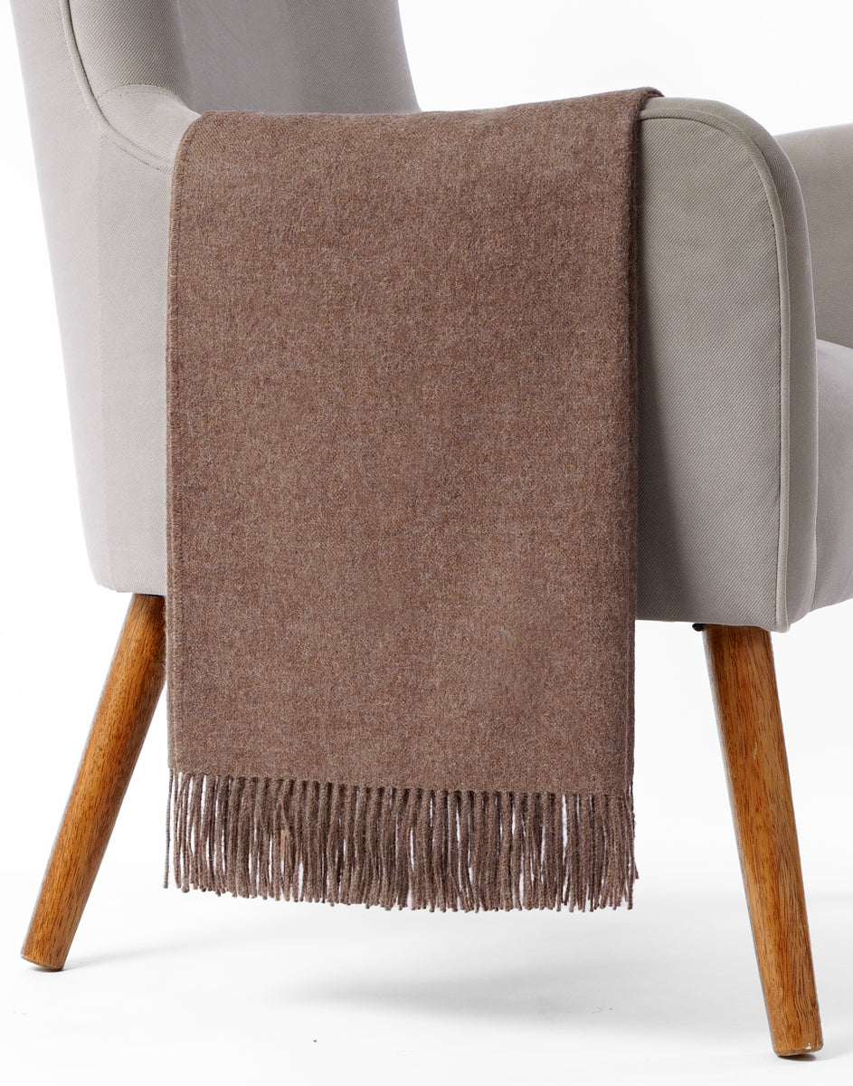 Manta chocolate de baby alpaca extendida sobre silla de madera clara